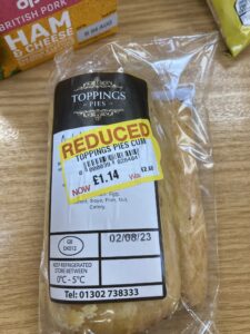 A Toppings brand Cumberland sausage roll, with the price label showing the unfortunately abbreviated description “Toppings Pies Cum”.